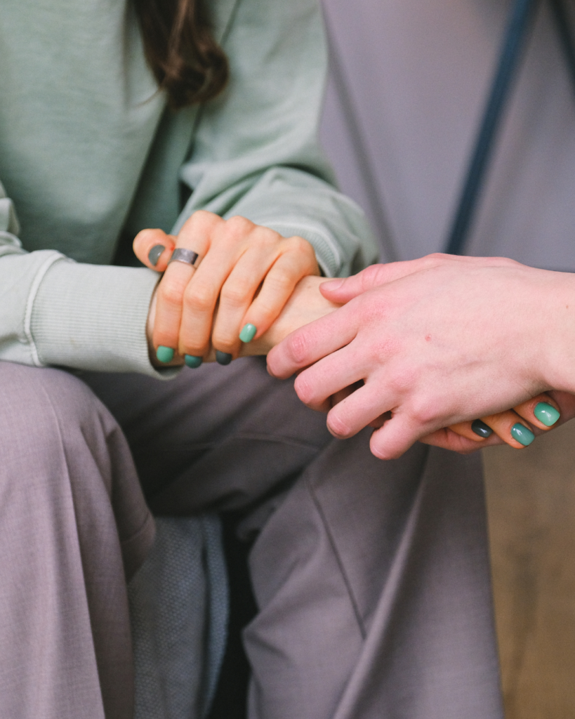 Image of hands holding each other in support. One hand has fingernails painted different shades of green.