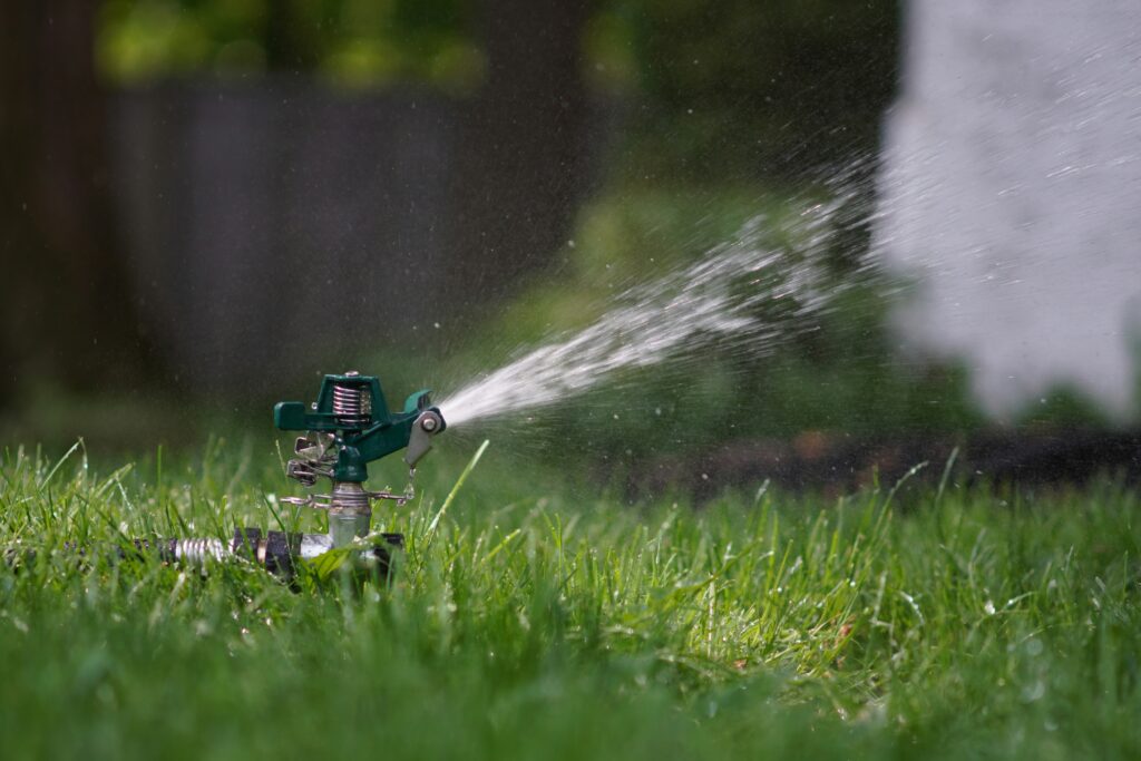 Image of a sprinkler spraying water over green grass.