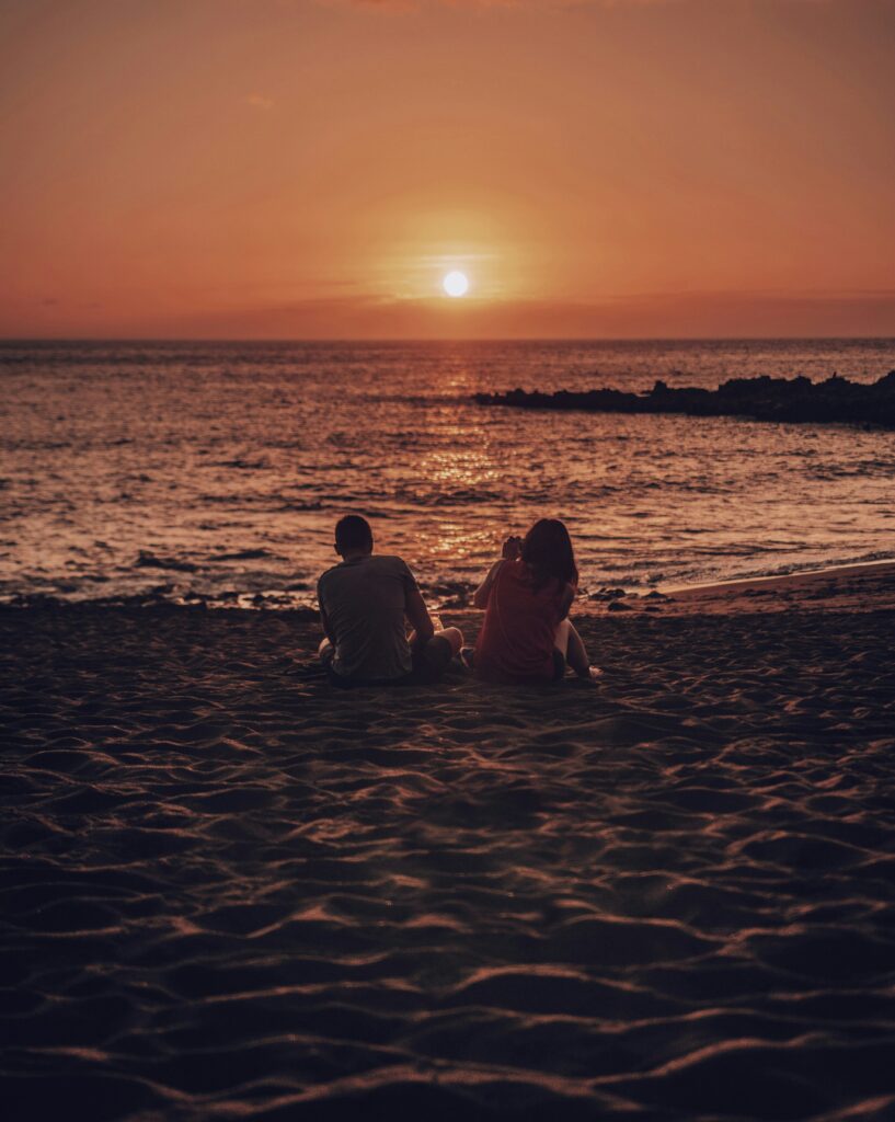 A couple sitting on a beach at sunset