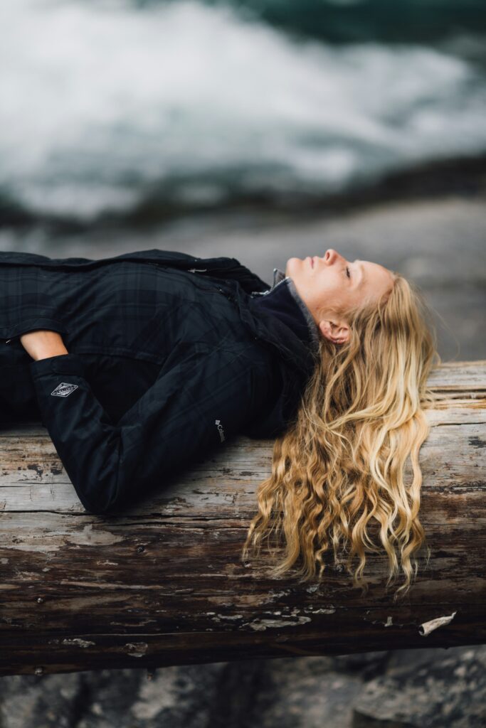 Image of a woman laying down on a log with her eyes closed.