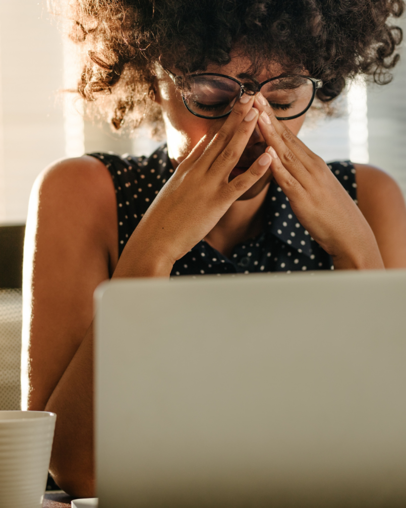 Image of a woman looking stressed sitting in front of a computer with her hands on her face